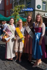 Vier Frauen in bayrischer Tracht und Schärpe und regionalen Produkten
